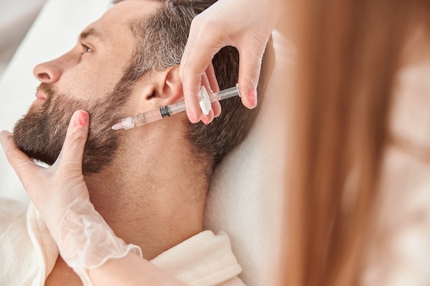 close up makes mesotherapy injections to beard man. treatment of male by a beautician for hair growth.