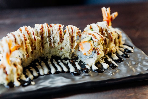 Foto close-up maki sushi met rijst, garnalen tempura, avocado en kaas in overdekte knapperige tempura bloem. topping met teriyakisaus en mayonaise.