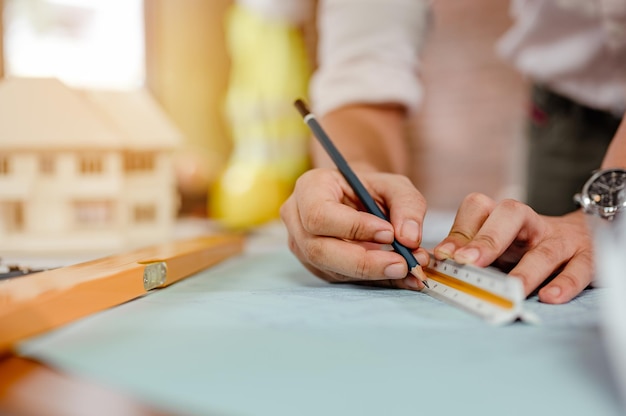 Close up of male architect hands measuring and making model house on the desk at sunset. Engineer, Engineering, Architecture, Design, Planning, Occupation concept.