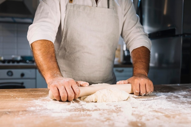 close up male baker s hand flattening dough with rolling pin