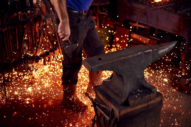 Close Up Of Male Blacksmith Holding Hammer Next To Anvil Surrounded By Sparks And Embers