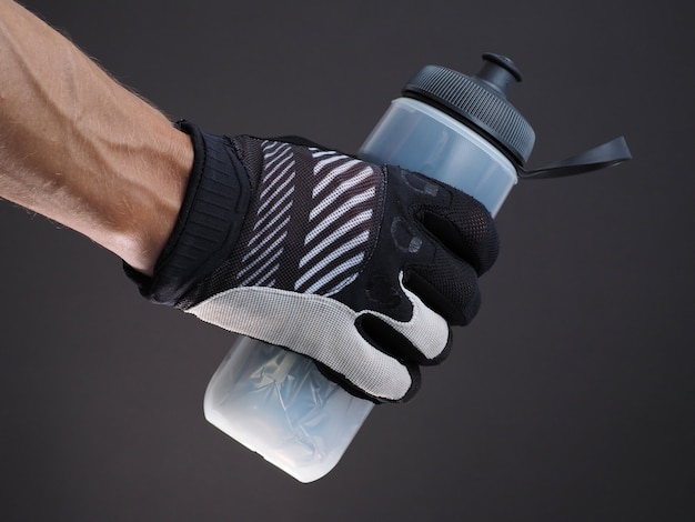 Крупным планом мужской велосипедист руки, держащей пластиковую термо бутылку воды на темном