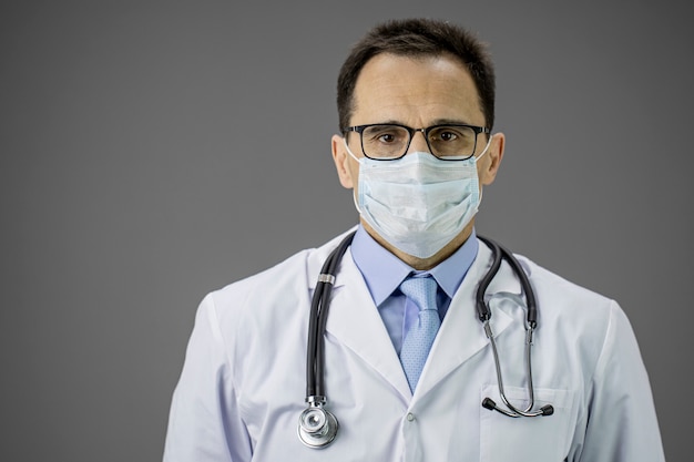 Close up male doctor in white coat, medical mask looks seriously. Copy space