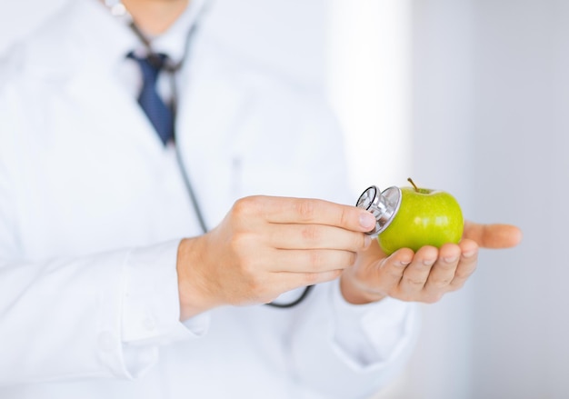 close up of male doctor with green apple and stethoscope