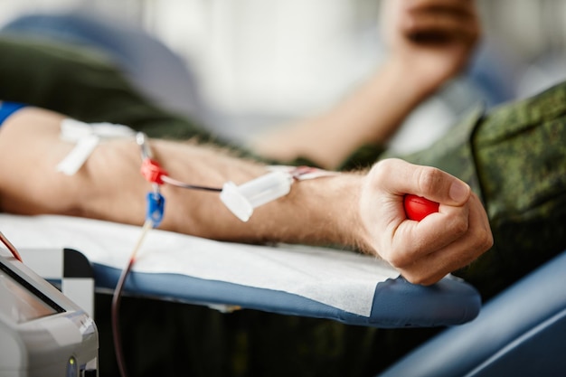 Photo close up of male donor giving blood and holding red stress ball in hand at donation center copy space