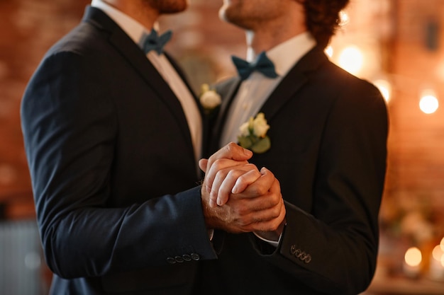 Primo piano di una coppia gay maschile che balla insieme durante la cerimonia di matrimonio e si tiene per mano lo spazio della copia