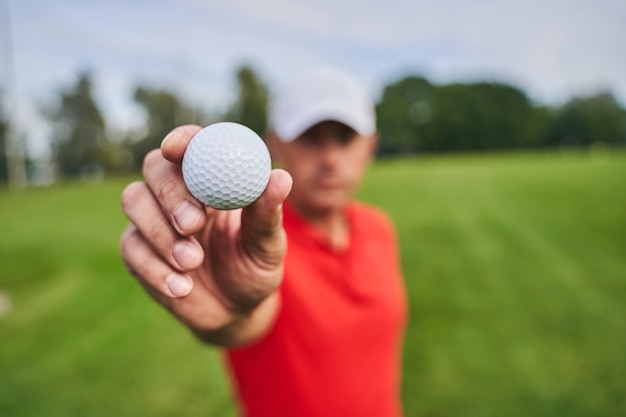 카메라 앞에서 흰색 골프 공을 보여주는 남성 손 클로즈업