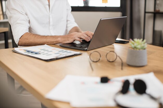 Foto primo piano della mano maschile in abbigliamento formale che digita su un computer portatile moderno mentre è seduto alla scrivania