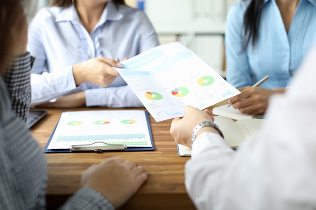 Close-up of male hand giving documents with diagram and graph to woman in blue blouse.