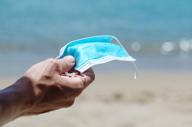 Close-Up Of Male Hand Holding Surgical Mask On The Beach.
