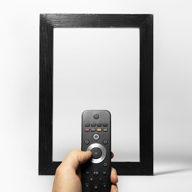 Close-up of male hand holding TV remote against black empty frame