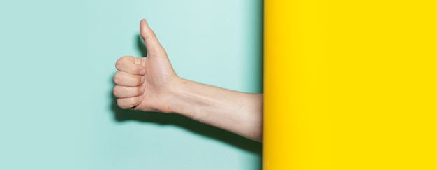 Крупный план мужской руки, показывающей большой палец вверх жест на двух фонах желтого и бирюзового цветов.