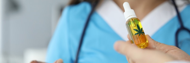 Close-up of male hands giving bottle of cannabinoid oil to doctor