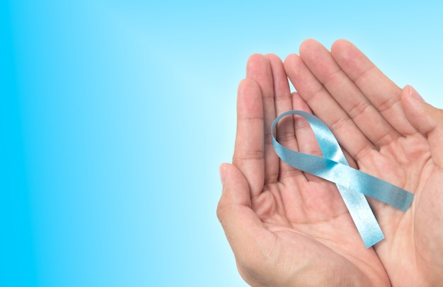 close up of male hands holding light blue ribbon for prostate cancer