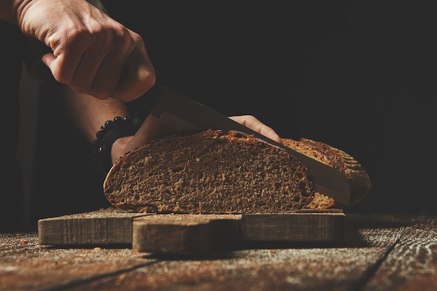 Close-up of male hands slice organic fresh bread on wooden board