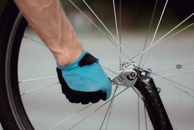 Close up of male hands in sport gloves fixing mountain bike,\
having breakdown while riding in the park
