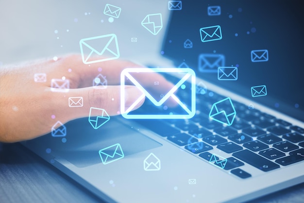 Close up of male hands using laptop keyboard on desk with glowing email letter icons on blurry background Communication and business message concept