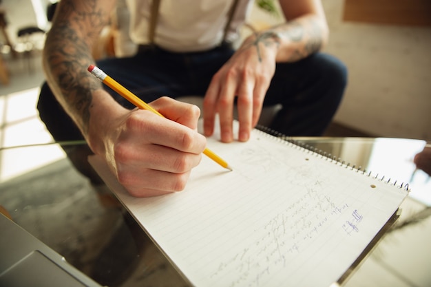 Primo piano di mani maschili che scrivono su un foglio vuoto sul tavolo di casa. prendere appunti, casa di lavoro, relazione per il suo lavoro. istruzione, freelance, arte e concetto di business. lascia la firma, facendo scartoffie.