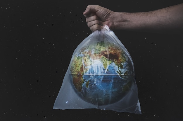 Close up male hold in plastic bag earth world globe on black\
background. save planet, planet is choking on plastic.. stop nature\
garbage, ecology environment protection concept. copy space.