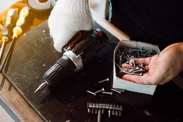 Close up of male mechanic holding electric cordless screwdriver\
drill with wood screw in the factory working with the screw\
professional carpenter concept furniture at home