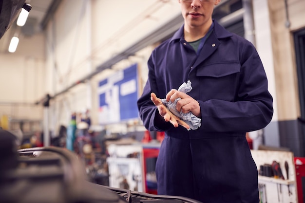 Primo piano del meccanico del motore maschio che pulisce le mani dopo aver lavorato sul motore dell'auto in garage