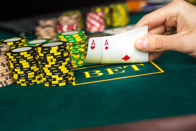 Primo piano del giocatore di poker maschio che solleva gli angoli di due carte assi al tavolo del casinò verde con assi