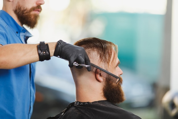 Close up of male professional hairdresser serving client by scissors