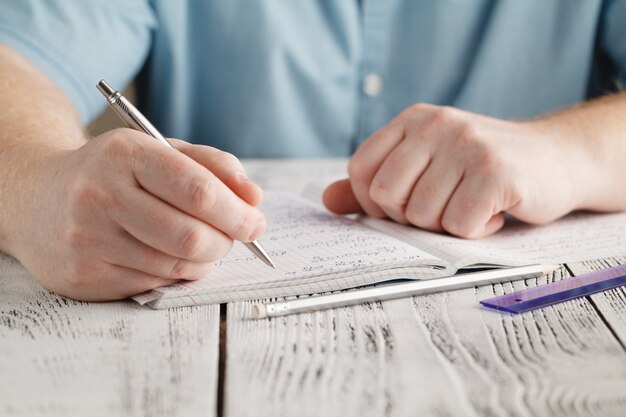 Close up male's hand writing on paper, writing messy math, student holding pen doing homework at home, calculate the results on paper , education concept