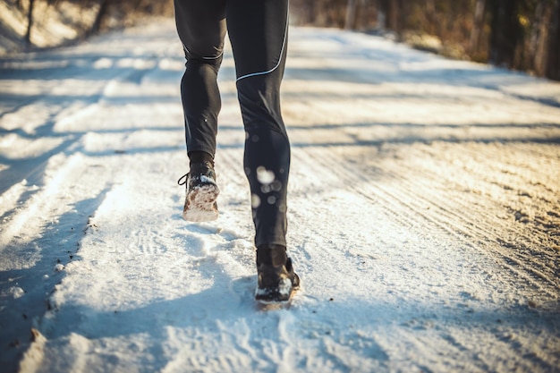 Close-up of a male's legs is running in the forest road during the winter training outside.