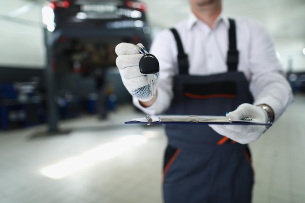 Close-up of male service worker give keys from fixed automobile to owner and maintenance documentation. Car service, professional mechanic, garage concept