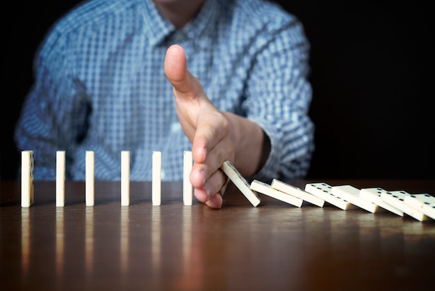 Close up male stop domino fall with hand on table on dark background f