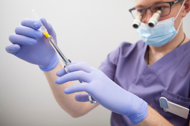 Close up of male surgeon holding anesthesia syringe, wearing microscope glasses