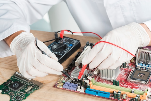 Foto primo piano di una scheda madre d'esame della mano maschio del tecnico con il multimetro digitale