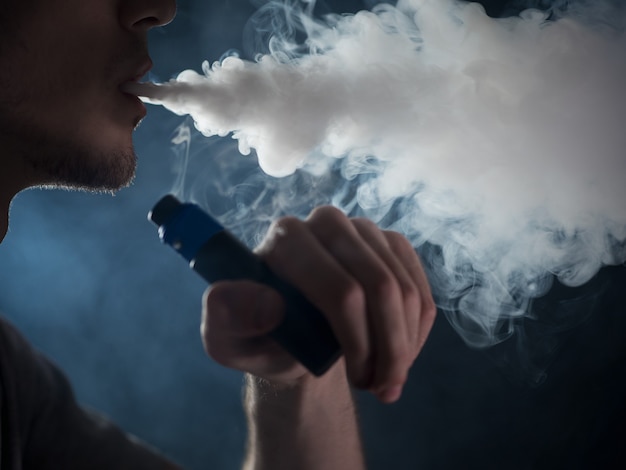 蒸気の雲を吐き出す男性のvaperのクローズアップ