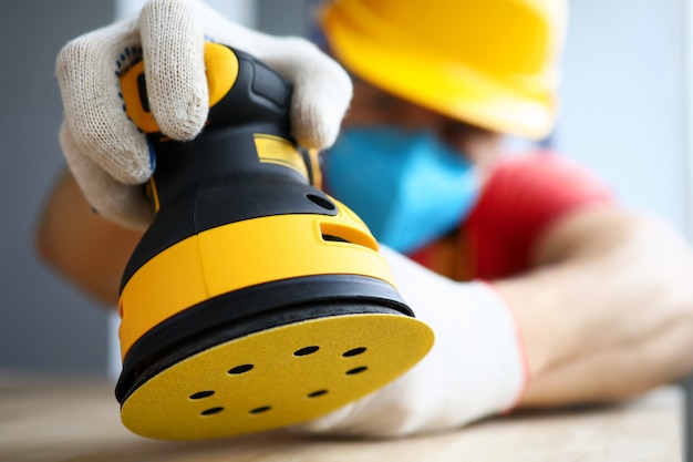 Close-up of male worker polishing piece of wood with modern electrical machine