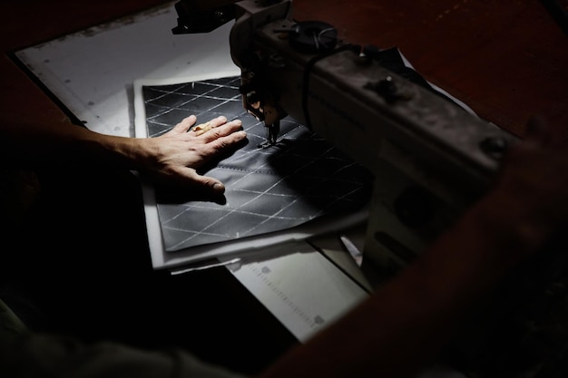 Close up of male worker sewing car upholstery detail with\
industrial sewing machine at factory accen