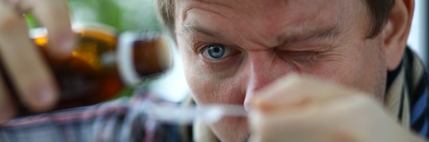 Close-up of males face carefully measuring cure from cough in spoon. Middle-aged man wearing scarf around neck.