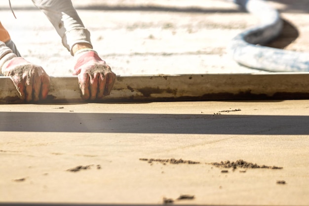 Close up of man builder placing screed rail on the floor covered with sandcement mix at construction site Male worker leveling surface with straight edge while screeding floor Blurred background