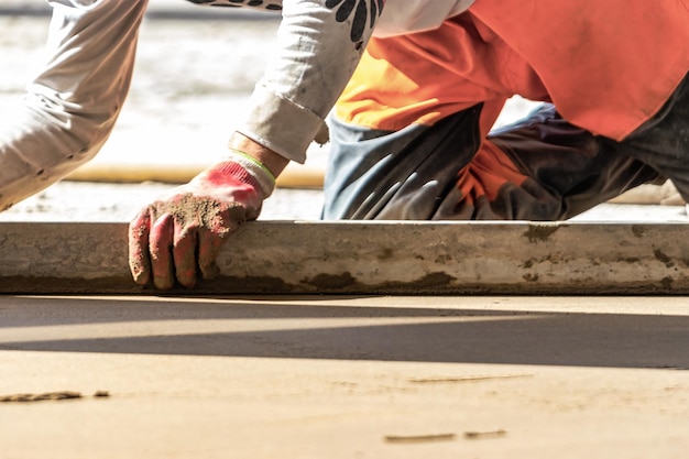 Primo piano del costruttore di uomini che posiziona la rotaia del massetto sul pavimento coperto con miscela di cemento in cantiere