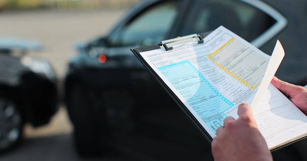 Close up of a man car insurance agent inspecting damaged car with agreed statement of facts on motor vehical accident form Male filling in a car repair claim Insurance concept