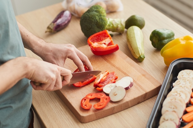 Primo piano dell'uomo che taglia le verdure fresche sul tagliere in cucina