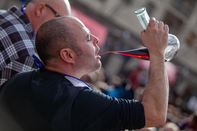 Close up of a man drinking red wine in a jar during an eating\
contest