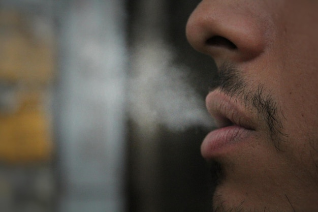 Foto close-up di un uomo che espira fumo
