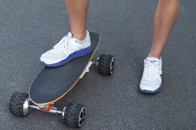 Chiuda in su dei piedi dell'uomo su skateboard elettrico moderno sulla strada su asfalto.