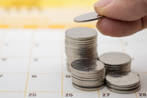 Close up of man finger holding coin and put to top of stack of coins on calendar