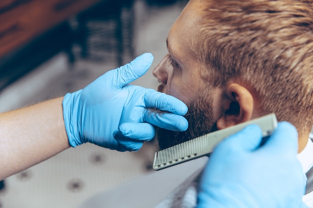 Close up man getting hair cut at the barbershop wearing mask during coronavirus pandemic. Professional barber wearing gloves. Covid-19, beauty, selfcare, style, healthcare and medicine concept.