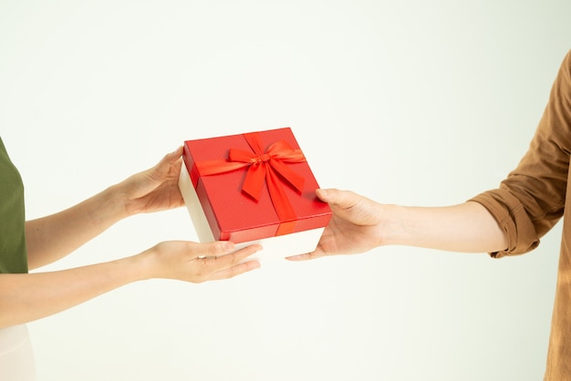 Close-up of man giving red gift box to woman over white wall