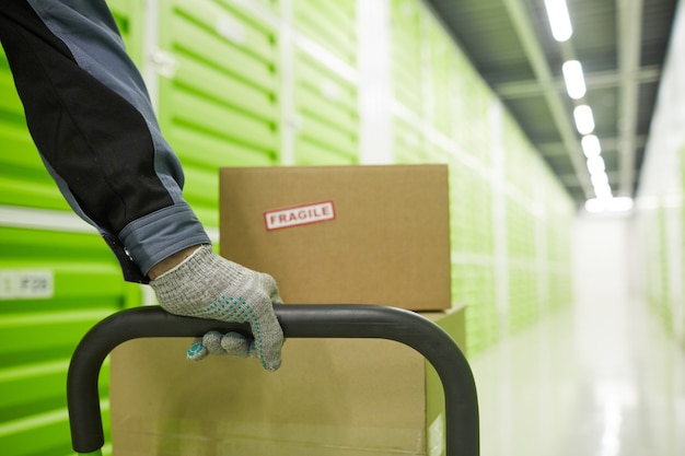 Close-up of man in gloves carrying trolley with parcels in warehouse