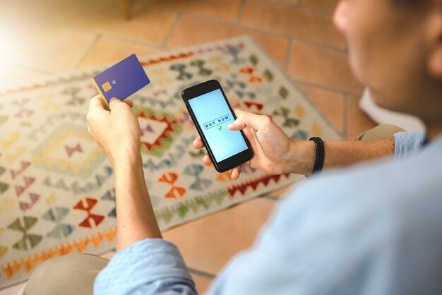 Close up  man hand doing shopping online with smartphone sitting on the sofa. Internet payment with credit card. Home banking and technology concept.