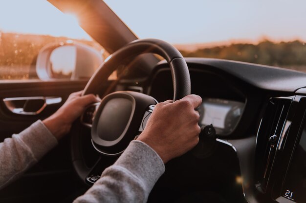 写真 夕暮れに車を運転する男の手を近づける. 車の旅の概念.